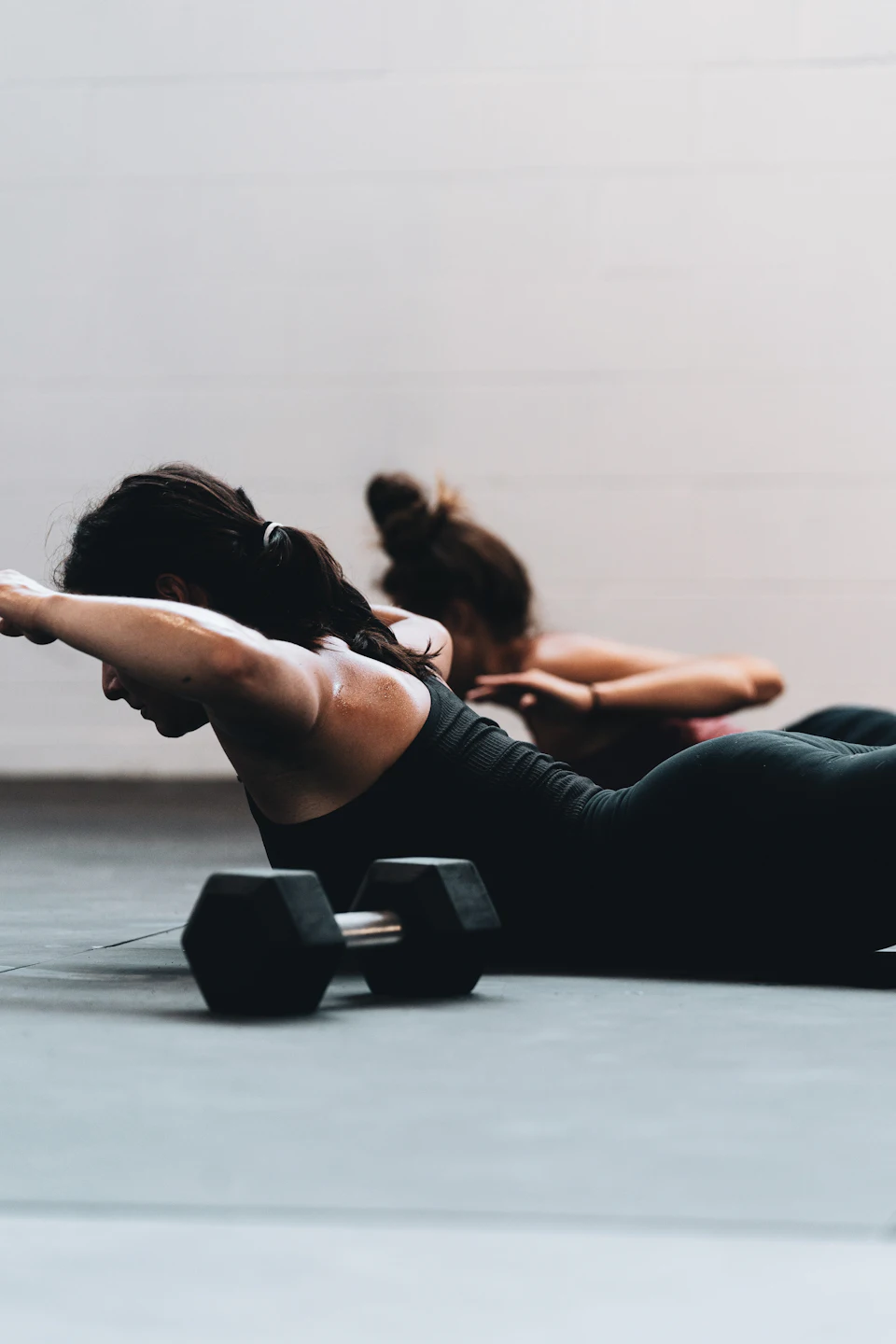 Woman in black tank top and black leggings lying on black floor