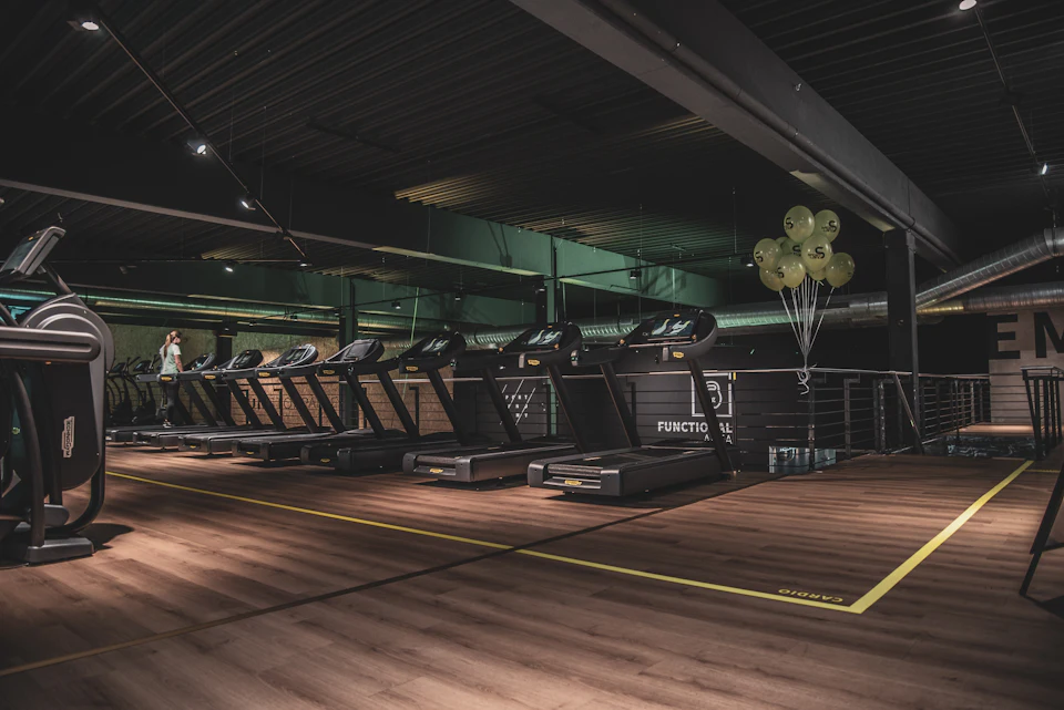 A row of treadmills in a gym with wooden floors and green balloons