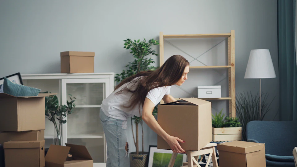 A woman moving boxes in a living room