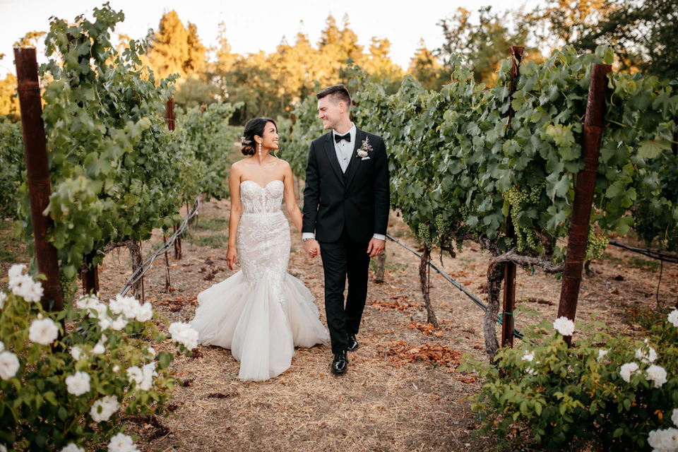 Newlyweds stroll through a sunny vineyard with white flowers