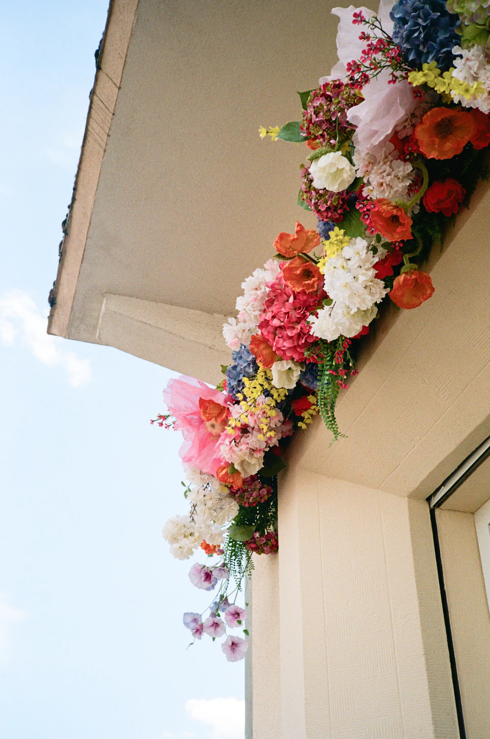 A colorful floral arrangement hanging from the corner of a beige building exterior